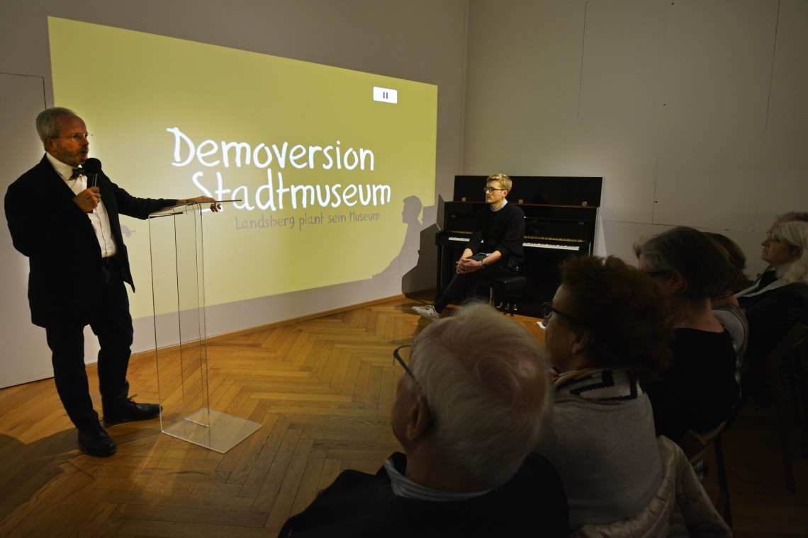 Axel Flörke hält eine Rede vor Publikum, im Hintergrund der Titel der Ausstellung &quot;Demoversion Stadtmuseum&quot;.