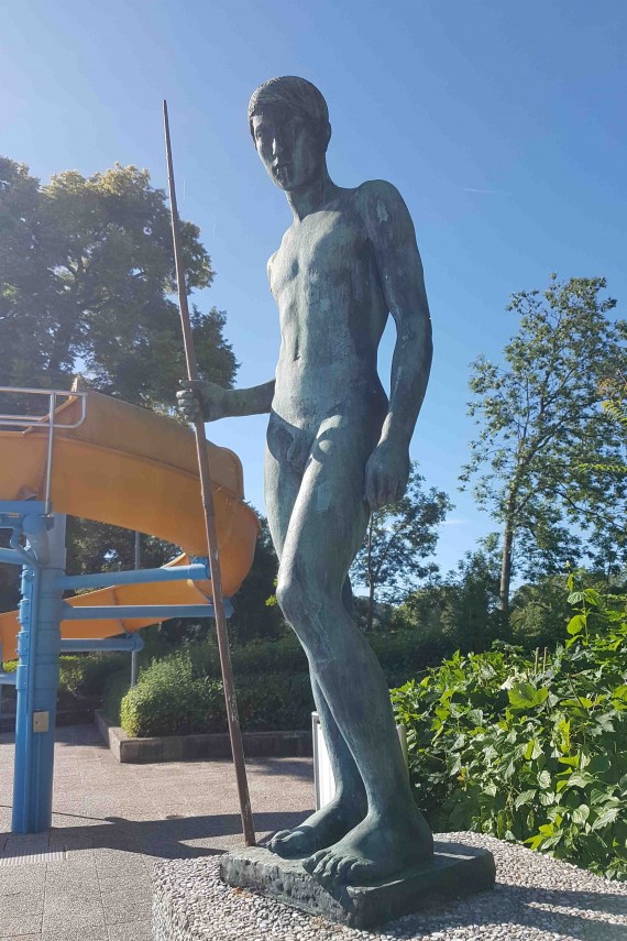 Skulptur eines jungen Mannes mit Speer neben einer Wasserrutsche im Inselbad