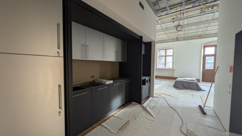 Links im Raum ist eine dunkelgraue Küchenzeile in eine Nische eingebaut.