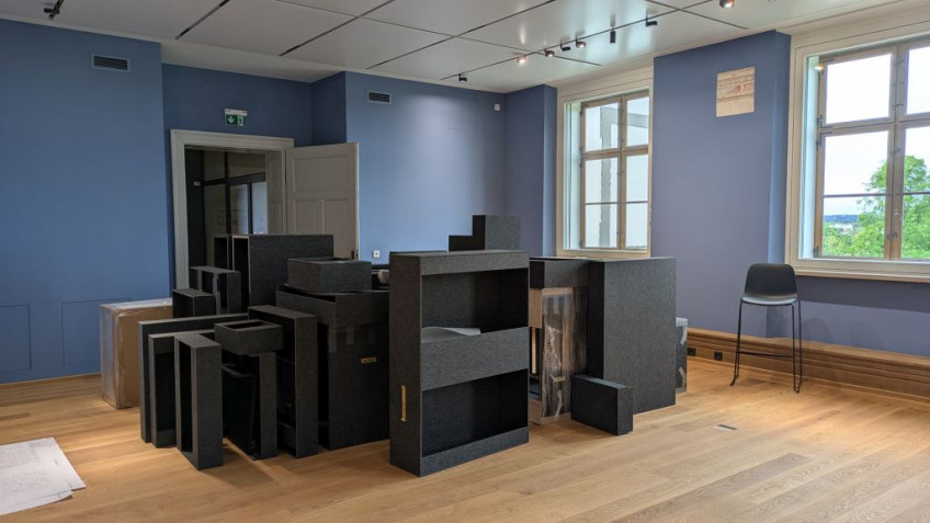 Graue Filzkästen in unterschiedlicher Größe stehen in der Mitte eines blau gestrichenen Ausstellungsraums.